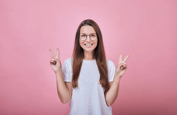 Cheerful girl in glasses and white T-shirt shows fingers peace — Stock Photo, Image