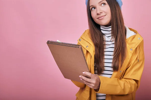 Söt utbildad flicka stående med anteckningsbok och penna i händerna eftertänksamt — Stockfoto