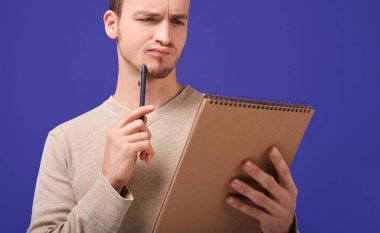 Thinking man with a brown paper notebook looks at page clipart