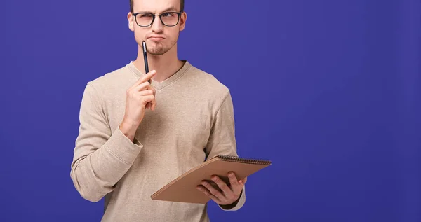 Pensive guy editor with a brown notebook and black pen near his face looks straight — Stock Photo, Image