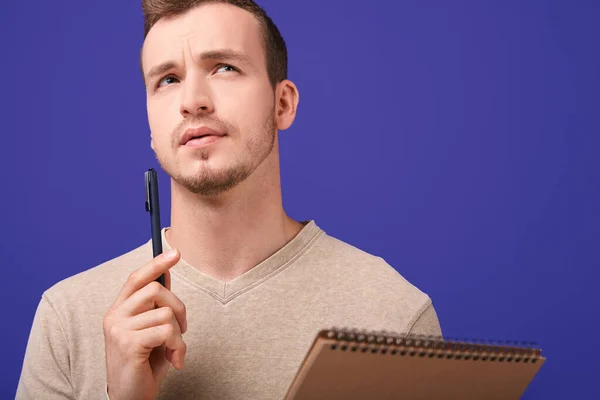 Thoughtful creator with paper notebook and ballpoint pen looking up — Stock Photo, Image