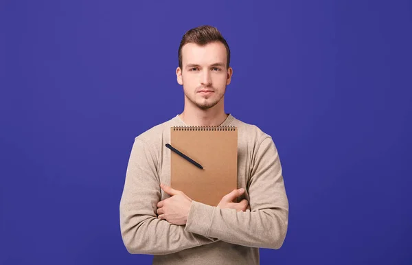 A young confident confident guy hugging a brown notebook with black ballpoint pen by hands — Stock Photo, Image