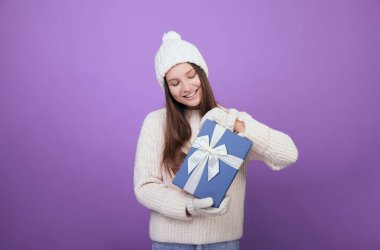 Beyaz şapkalı ve eldivenli bir kız elinde bir hediye tutuyor..