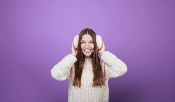 A smiling girl holds on to the fur headphones on her head. — Stock Photo, Image