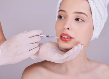 A cosmetologist doctor makes an injection on the lips of a young girl.