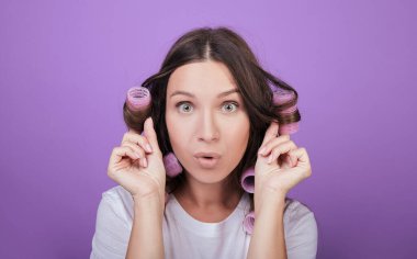 Çekici kahverengi saçlı kadın başını bigudilerle tutuyor.