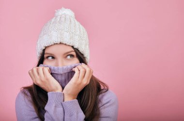 Kar beyazı şapkasının altında siyah dalgalı saçları olan sevimli bir kız yana bakıyor..