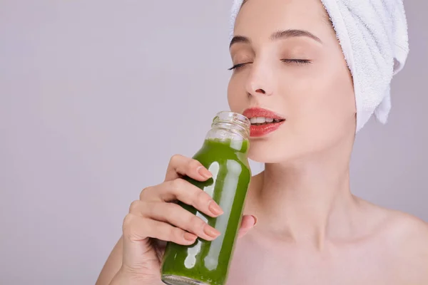 Linda senhora depois de um chuveiro goza de um smoothie verde em uma garrafa . — Fotografia de Stock