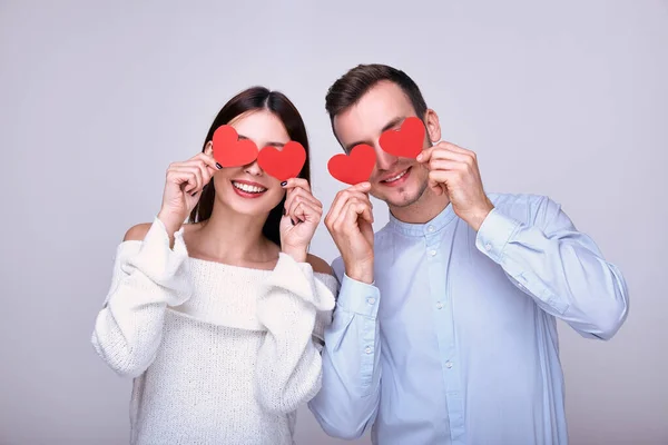Cute cute girl and mischievous cheerful guy are holding red hearts near their eyes — Stock Photo, Image