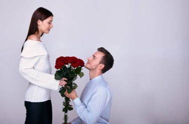 Genç bir aşık dizlerinin üzerine çöker ve kız arkadaşına kırmızı güller verir..