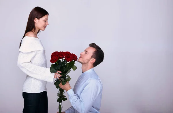 A young lover stands on one knee and gives his girlfriend red roses. — Stock Photo, Image