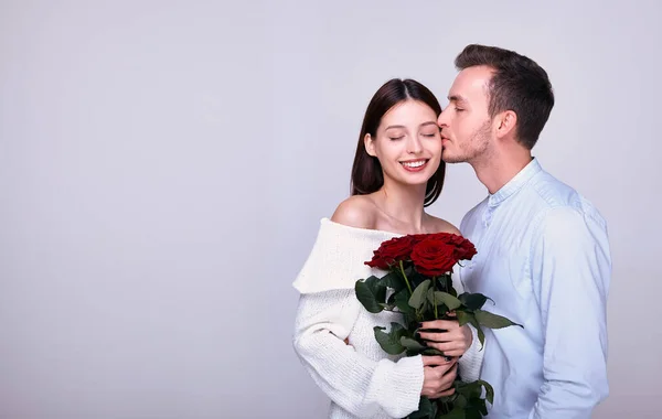 A young guy gives roses to his beautiful girlfriend and kisses her. — Stock Photo, Image