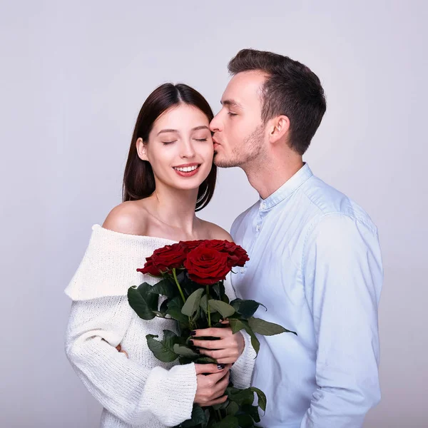 Handsome elegant guy is giving roses to his beautiful girlfriend and kissing her. — Stock Photo, Image