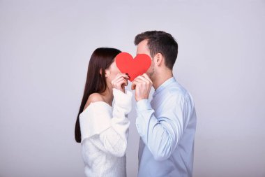Genç ve güzel bir çift kırmızı bir kalple yüzlerini kapatıyor.