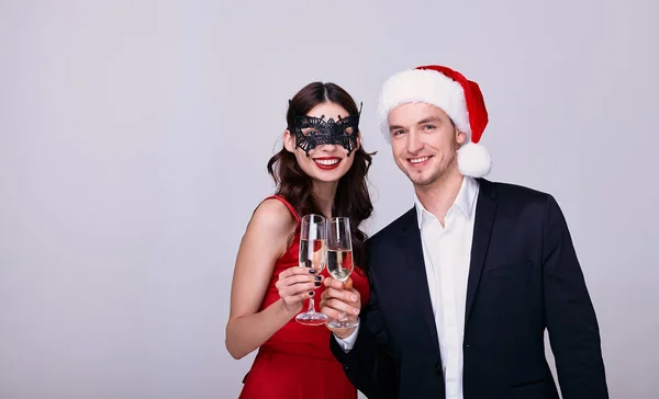 Happy young couple at the carnival drink champagne and celebrate the new year. A lady in a red dress and a guy in a Santa hat is drinking champagne on a white background.