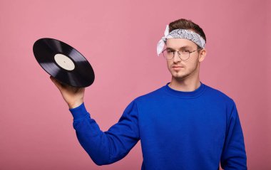 Vinil 'e odaklan. Yakın plan. Koyu mavi ceketli havalı bir adam elinde siyah bir plakla pembe arka planda duruyor. Gençlik, gençlik, tarz, güven, neşe, sakinlik.