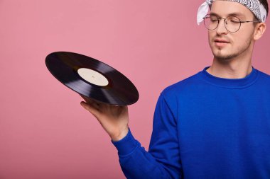 Vinil 'e odaklan. Yakın plan. Koyu mavi ceketli havalı bir adam elinde siyah bir plakla pembe arka planda duruyor. Gençlik, gençlik, tarz, güven, neşe, neşe.