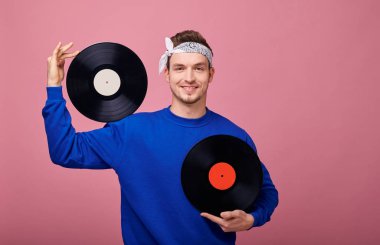 Retro tarzı gülümseyen beyaz bandanalı, mavi kazaklı hippi bir siyah plağı omuzunda tutuyor ve ikinci rekoru göğsünde tutuyor. Yakın plan. Mutlu, neşeli.