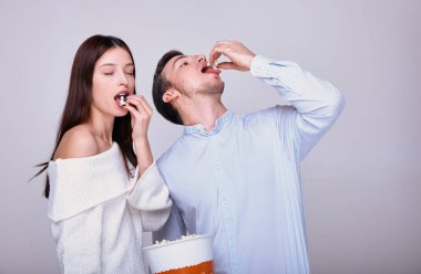 Gri arka planda genç bir çift patlamış mısır yiyor. Kız tatmin olmak için gözlerini kapadı ve adam direk ağzına patlamış mısır attı. Aile hafta sonu. Sinema ve tiyatro. Birlikte zaman geçirmek.