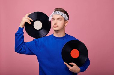 Yakın plan. Koyu mavi ceketli havalı bir adam elinde siyah bir plakla pembe arka planda duruyor. Gençlik, tarz, neşe, neşeli ruh hali. Retro biçimi.