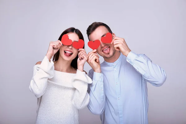Couple incroyablement étonnant d'amoureux tenant des cœurs en carton rouge dans les mains près de leurs yeux, fête de la Saint-Valentin . — Photo
