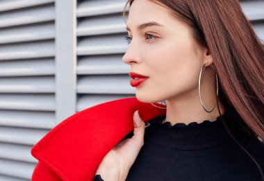 Cazip kız sakince yan bakıyor, omzunun üzerinden kırmızı bir ceket atıyor.