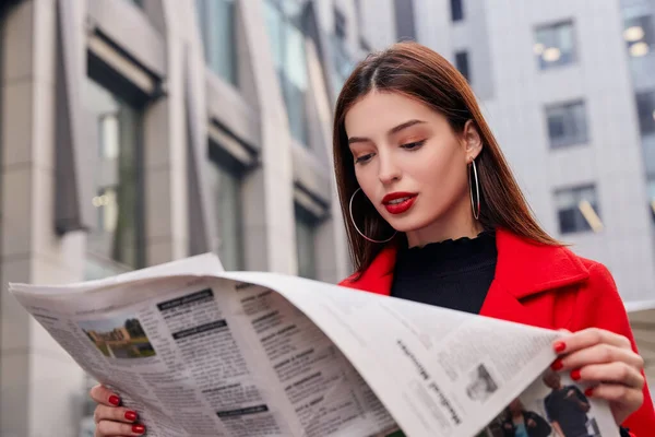 穿着黑色高尔夫和戴耳环的红色秋衣的漂亮迷人女士正在看新鲜的报纸 — 图库照片