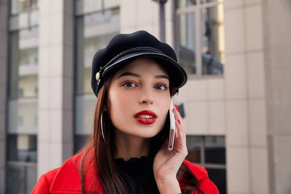 Cryptic charming lady with red lips in kepi talks on cellphone and looks at you enigmatically — 图库照片
