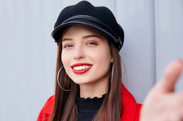 Dulcemente bonita señora seductora con una sonrisa encantadora en abrigo de otoño rojo y kepi hace selfie — Foto de Stock