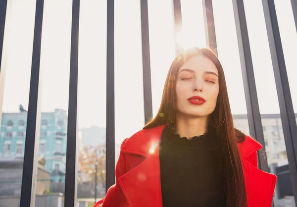 Sun\'s rays are breaking through the back of engaging sweet lady in red coat and sun above her head