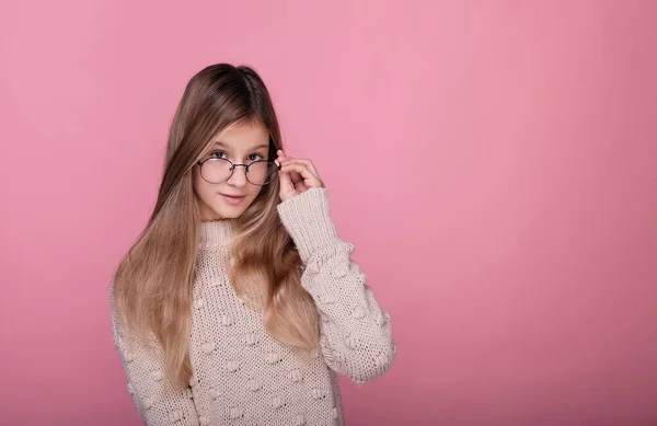 Cute young girl in a sweater and round glasses on a pink background. — Stock Photo, Image