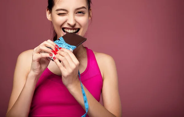 A girl in a sports uniform eats chocolate with pleasure. — Stock Photo, Image