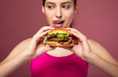 Aç kadın elinde koca bir hamburger tutuyor..