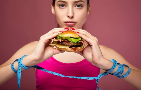 Close-up of tied hands with a measuring tape with a burger. — Stock Photo, Image