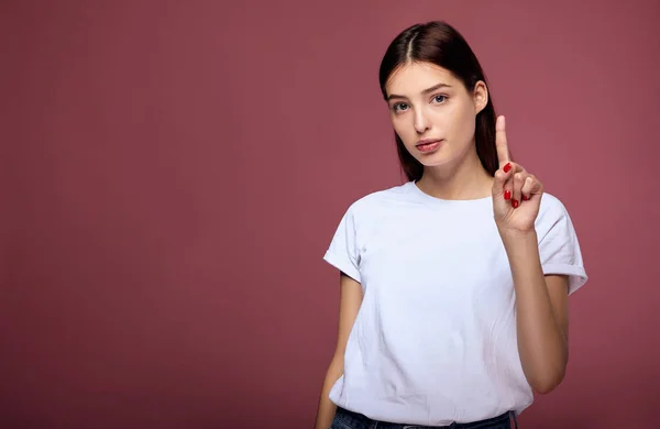 Cheerful young lady raises finger above stands against pink background. — Stock Photo, Image