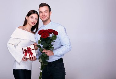 Çiçekleri olan ve arka planda poz veren neşeli, genç bir çift..