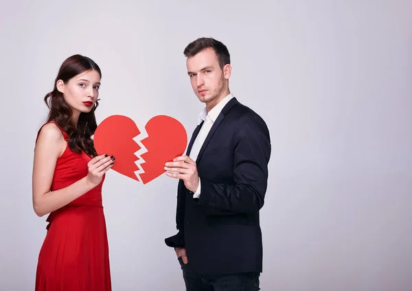 Un corazón rojo roto en las manos de una pareja joven y elegante sobre un fondo blanco . —  Fotos de Stock