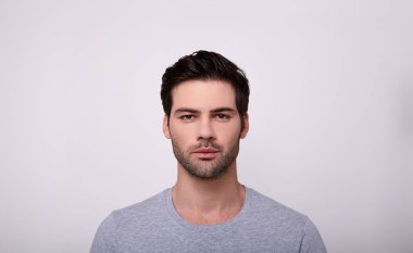 Genç adam gri arka planda dururken kameraya bakıyor..