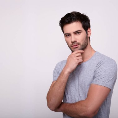 Yakışıklı genç adam kameraya bakıyor ve elini çenesinde tutuyor..