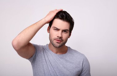 Gri tişörtlü beyaz bir adam saçını düzeltiyor..