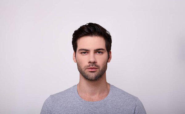 Young man looking at camera while standing against grey background.