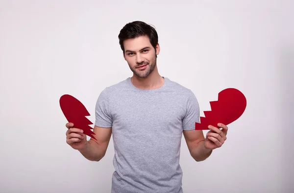 Homem bonito encantador com um coração vermelho partido em um fundo branco . — Fotografia de Stock