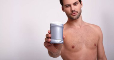 Vahşi güzellik. Güçlü adam sağ elinde gri deodorant tutuyor ve çerçeveye bakıyor.