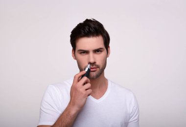 Elinde budayıcı olan yakışıklı beyaz adam burnundaki kılları alıyor..