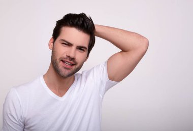 Yüzünü çeviren ve ellerini başının arkasında tutan bir adam gri arka planda duruyor..