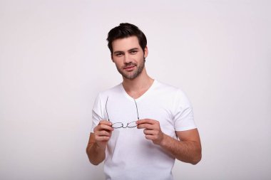 Ciddi özgüvenli sakallı erkek kameraya gizemli bir ifadeyle bakıyor, beyaz arka planda büyük gözlük takıyor..