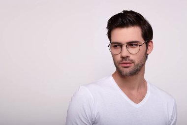 Gözlüklü, beyaz tişörtlü, yakışıklı bir maço beyaz arka planda düşünceli bir şekilde duruyor..
