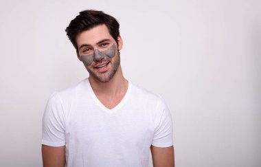 Beyaz bir arka planda yüzünde maske olan gülümseyen beyaz bir genç..