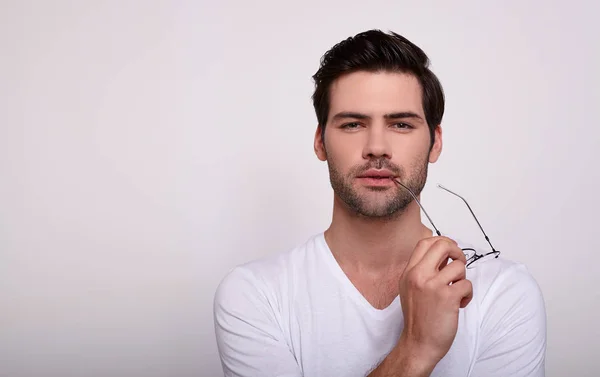 Um jovem bonito com um corte de cabelo na moda em uma camiseta branca está segurando óculos para a vista em suas mãos . — Fotografia de Stock