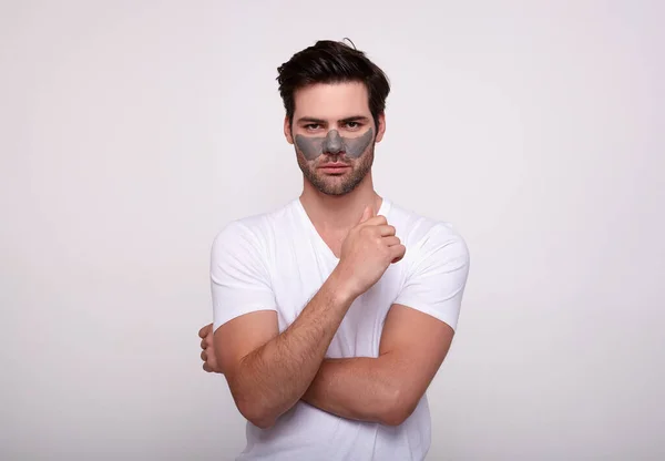 Een jonge serieuze macho maakt cosmetische ingrepen voor het gezicht staande op een witte achtergrond. — Stockfoto